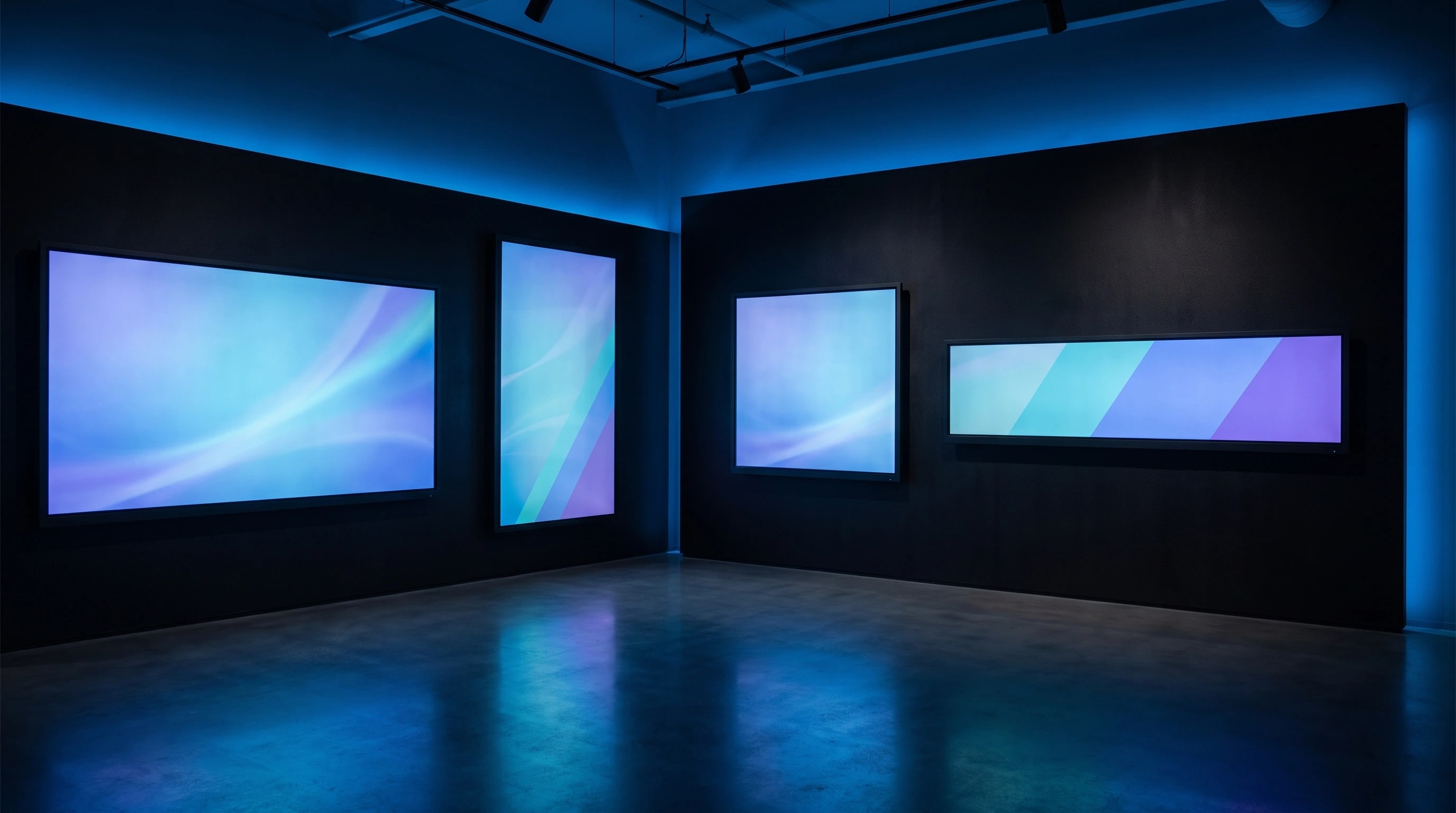 Sala espositiva buia con quattro display di formati diversi accesi contemporaneamente su una parete nera.